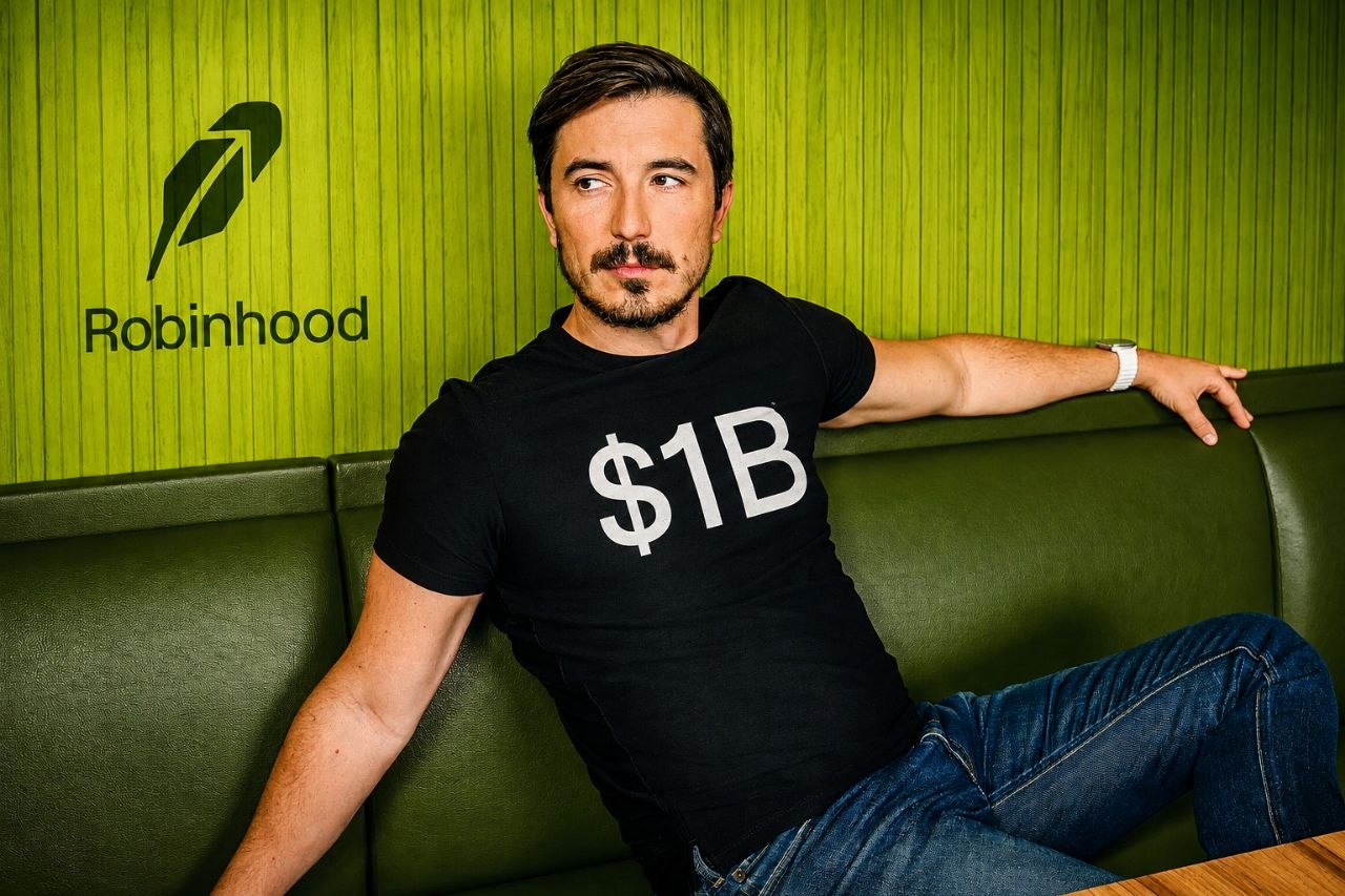 Vlad Tenev wearing a $1B shirt in front of a Robinhood wall
